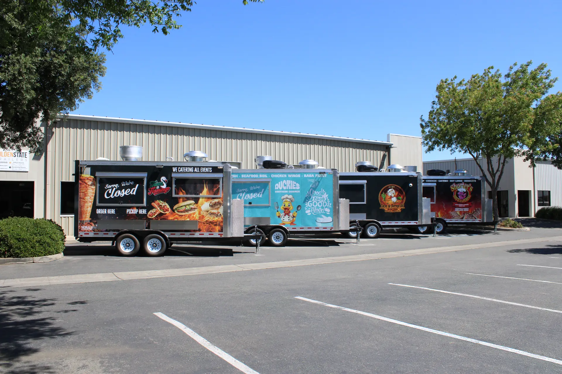 Four finished custom food trailers with full-color wraps parked outside the Golden State Trailers factory