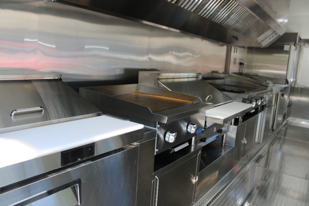 Commercial griddle station under ventilation hood inside school food trailer