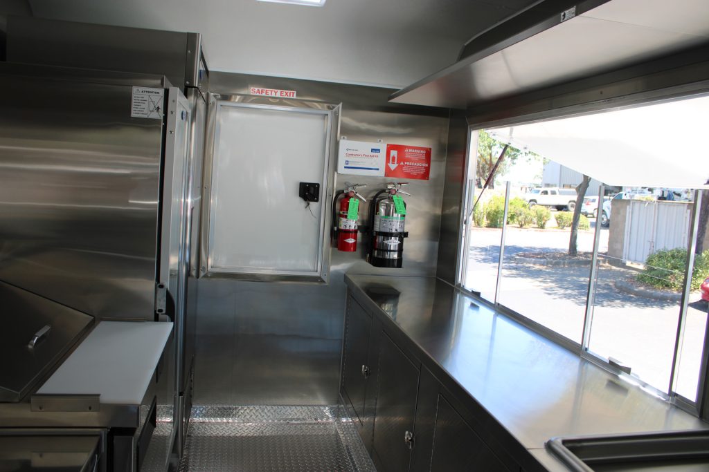 Interior of The Salty Buccaneer 22-ft school food trailer with stainless steel counters, enclosed storage, service window, and safety exit