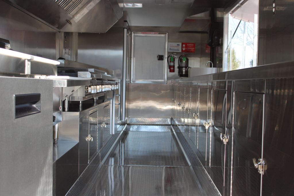 Cougar’s Grill 24-ft school food trailer interior with stainless steel workstations, storage, cooking line, and central aisle