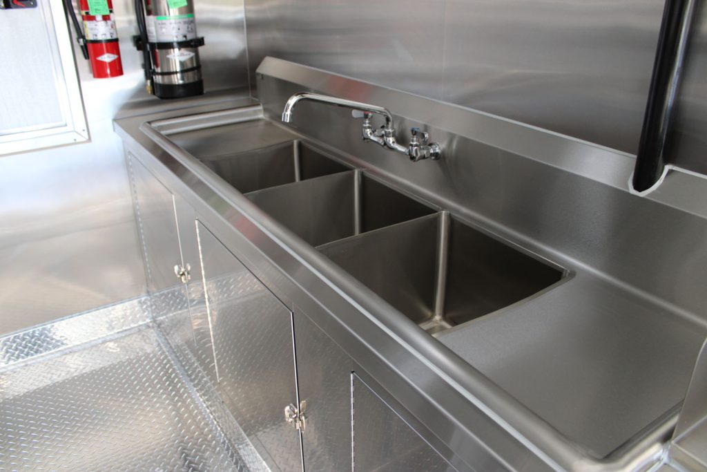 Stainless steel warewashing area inside Cougar’s Grill with a commercial three-compartment sink and adjacent work surface.