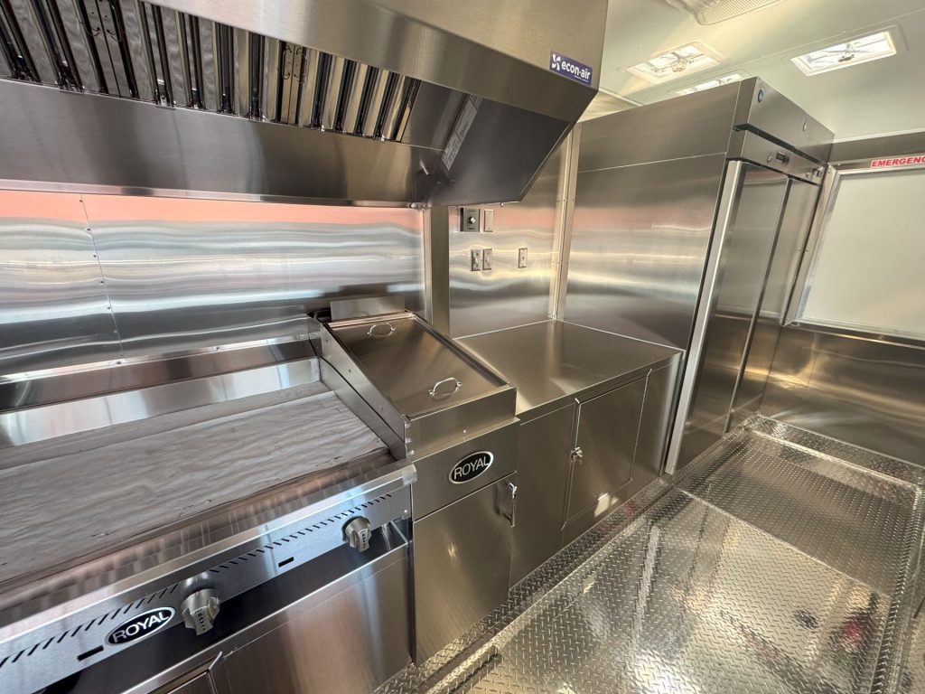 Commercial cooking line beneath ventilation hood inside Cougar’s Grill school food trailer