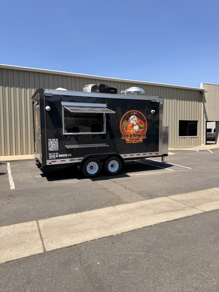 Custom food trailer exterior with tandem commercial-grade axles, branded wrap, service window, rooftop ventilation, and front utility enclosure.