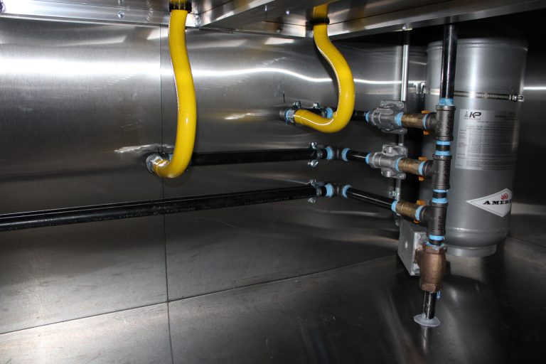 Commercial gas line installation inside food trailer with mobile kitchen rated flexible gas hoses, shutoff valves, and integrated fire suppression system cylinder for cooking equipment safety
