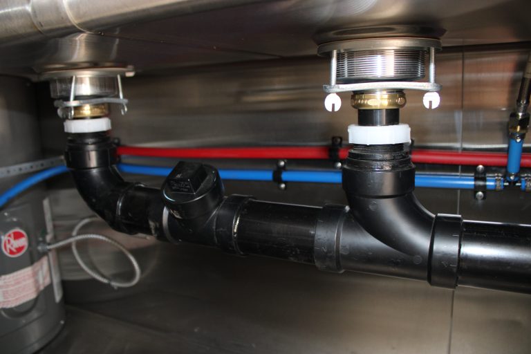 Commercial-grade plumbing system under food trailer sink with properly sized ABS drain lines, P-trap assembly, and hot and cold water supply lines