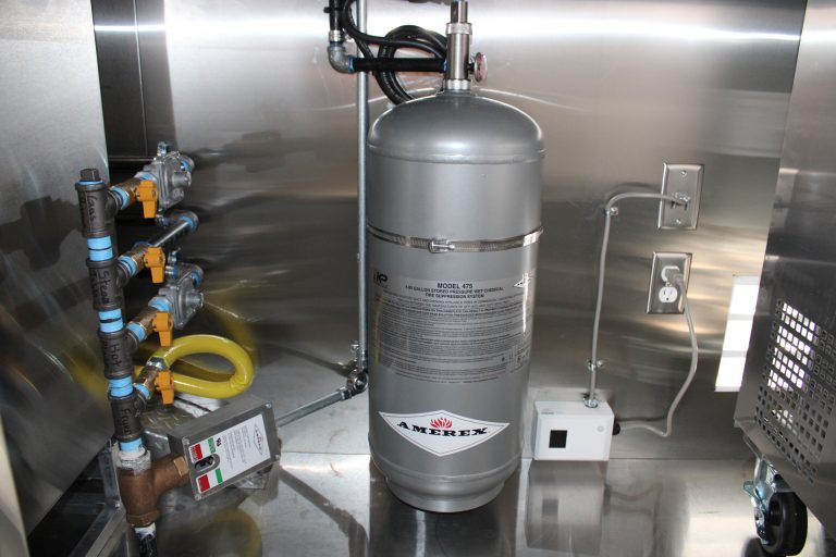 Commercial kitchen fire suppression system with agent tank, gas shut off valve and gas leak detector installed in stainless cabinet.