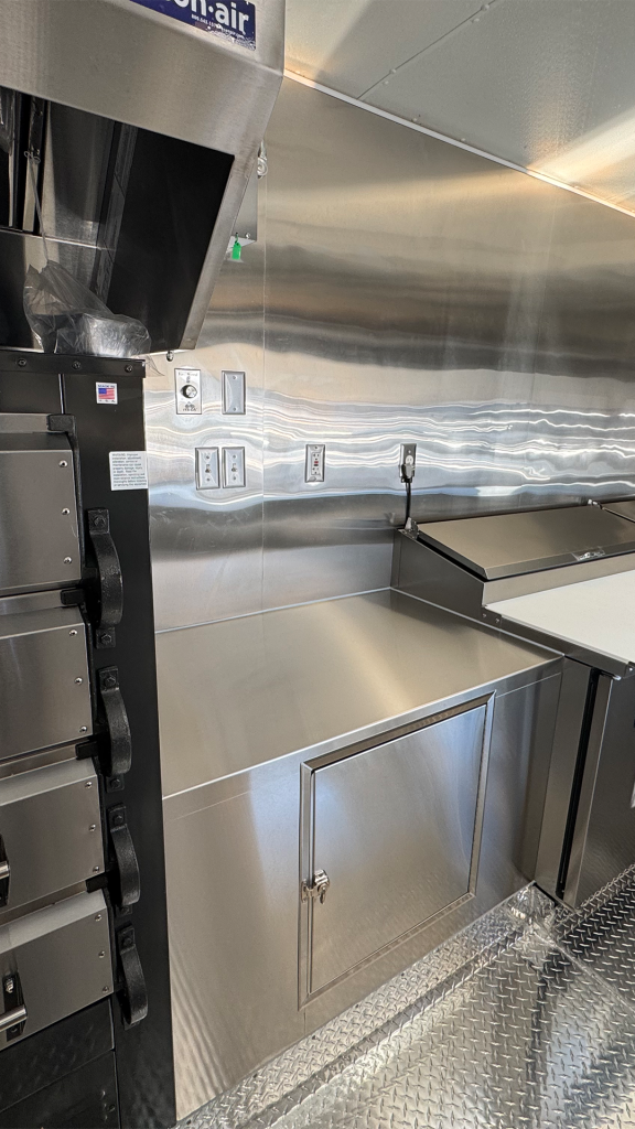 Custom food trailer electrical system with concealed wiring, stainless steel walls, outlets, work surfaces, and commercial kitchen equipment.