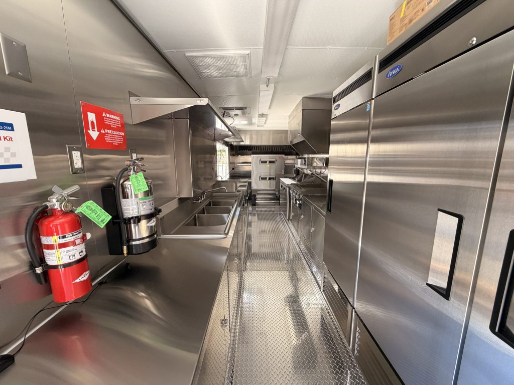 commercial pizza food trailer interior with three-compartment sink, handwashing area, stainless steel surfaces, and safety equipment