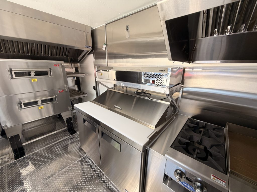custom pizza food trailer interior with double-stack conveyor oven, hot plates, griddle, stainless steel prep equipment, and commercial ventilation hoods