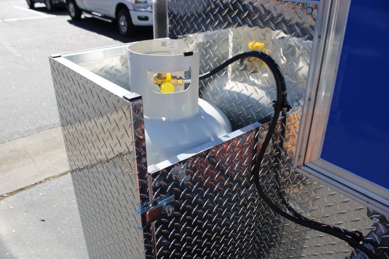 Food trailer propane tank with top fill valve mounted in aluminum diamond plate enclosure and connected to the LP gas system for commercial kitchen equipment