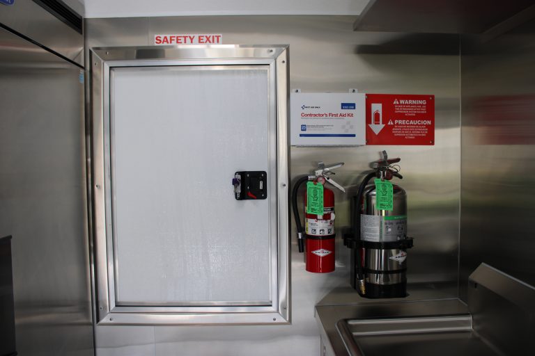 Food trailer safety exit door with fire extinguishers, first aid kit and safety warning signs.