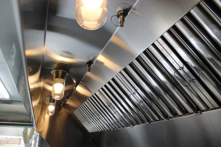 Food trailer stainless steel exhaust hood with grease filters, fire suppression nozzles and heat-resistant lighting installed above cooking equipment.