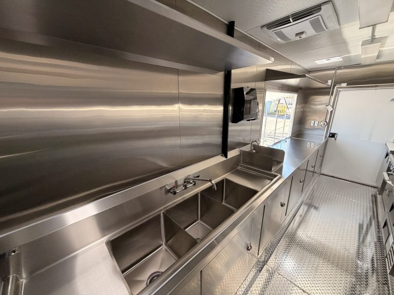 Limitless Kitchen food trailer stainless steel prep shelf above three-compartment sink with hand wash sink, HVAC vent and welded cabinet base