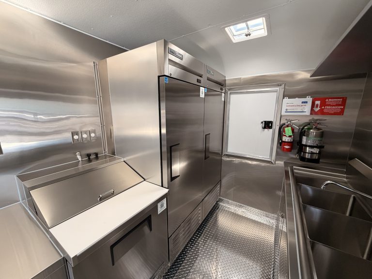 Smashed Broz Burgers food trailer rear zone with full-size reach-in refrigerator, hand wash sink, fire suppression system, rear entry door and welded stainless steel cabinets
