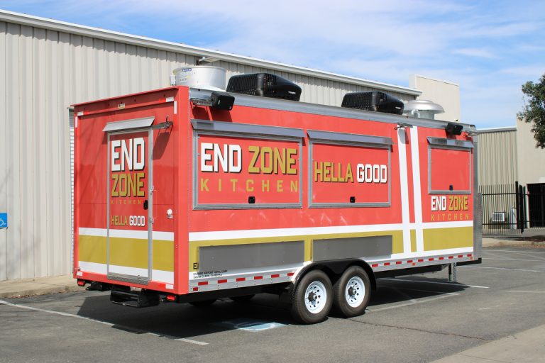 End Zone Kitchen 22ft food trailer rear three-quarter view with bold red gold 3M wrap, Hella Good branding, rear entry door and dual rooftop units, Golden State Trailers