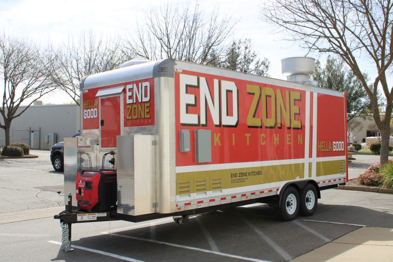 End Zone Kitchen 22ft food trailer front three-quarter view with bold End Zone Kitchen logo, red gold 3M wrap, generator compartment and tongue jack, Golden State Trailers
