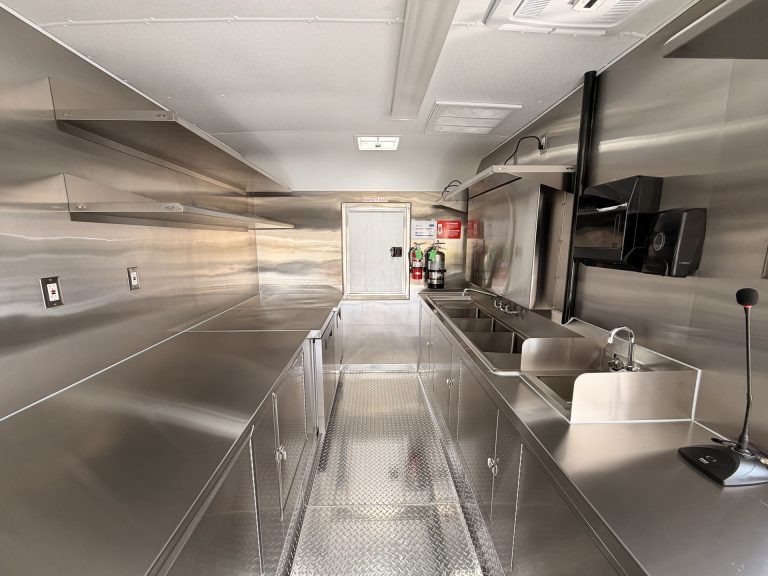 End Zone Kitchen food trailer interior view toward rear with three-compartment sink, hand wash sink, fire suppression system and stainless steel prep counters throughout
