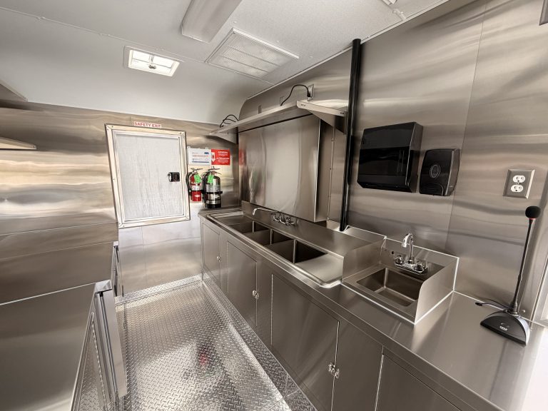 End Zone Kitchen food trailer rear zone with three-compartment sink, hand wash sink, microwave, fire extinguisher, rear entry door and welded stainless steel cabinets