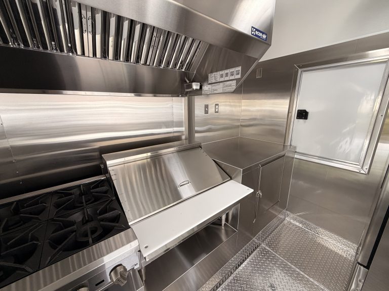 Mya's Teriyaki food trailer rear kitchen zone with commercial gas range, stainless steel splash guard, exhaust hood and rear entry door access