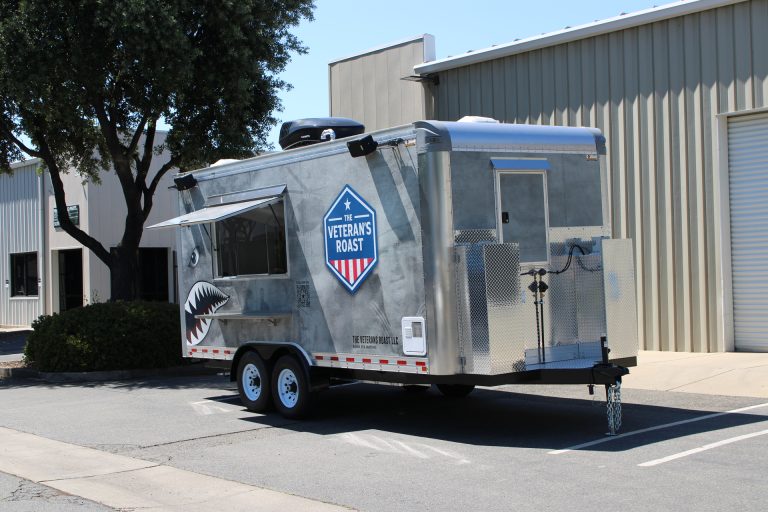 Front passenger side angle of 18ft American food trailer with military wrap and aluminum storage