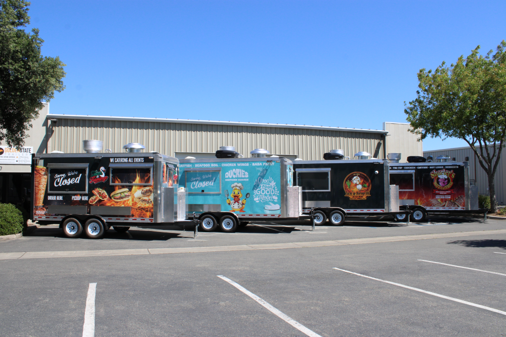 Row of custom food truck wraps on trailers of different sizes parked side by side