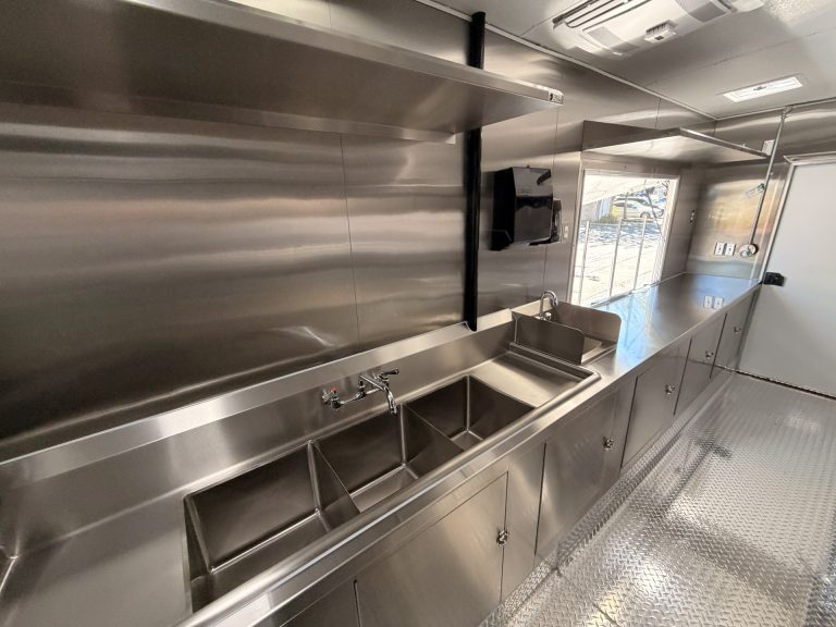 Shorter's BBQ and Catering food trailer stainless steel prep shelf above three-compartment sink, hand wash sink and welded cabinet base with serving window view