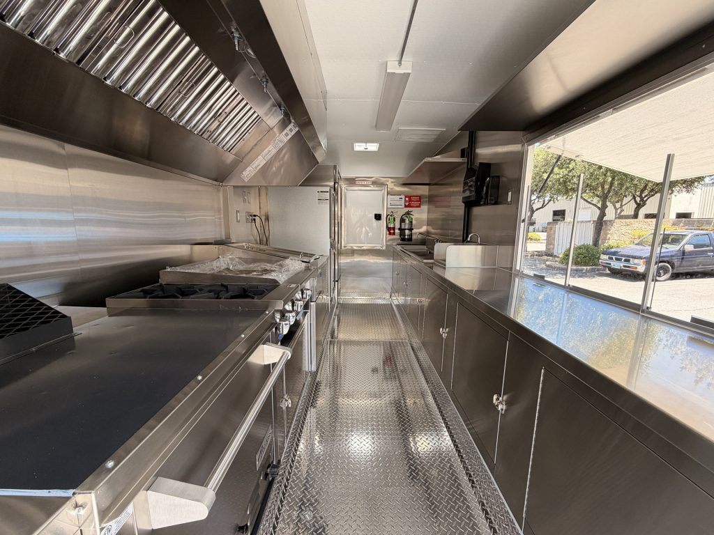 Custom food trailer interior with stainless steel cooking equipment and ventilation hood