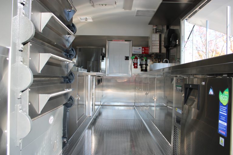 Interior kitchen aisle inside 16ft pizza food trailer with pizza ovens and stainless steel counters
