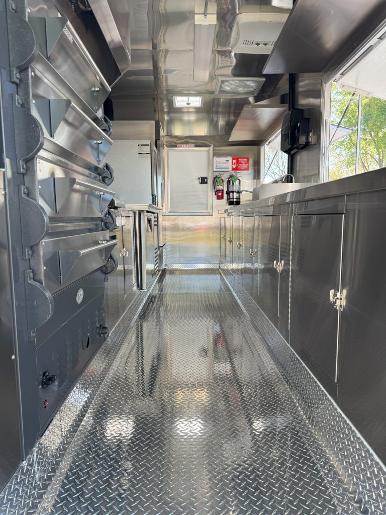 Interior kitchen aisle inside 16ft golf course food trailer with pizza ovens and stainless steel counters