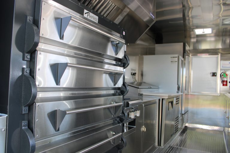 Commercial pizza oven and stainless steel prep area inside 16ft golf course food trailer