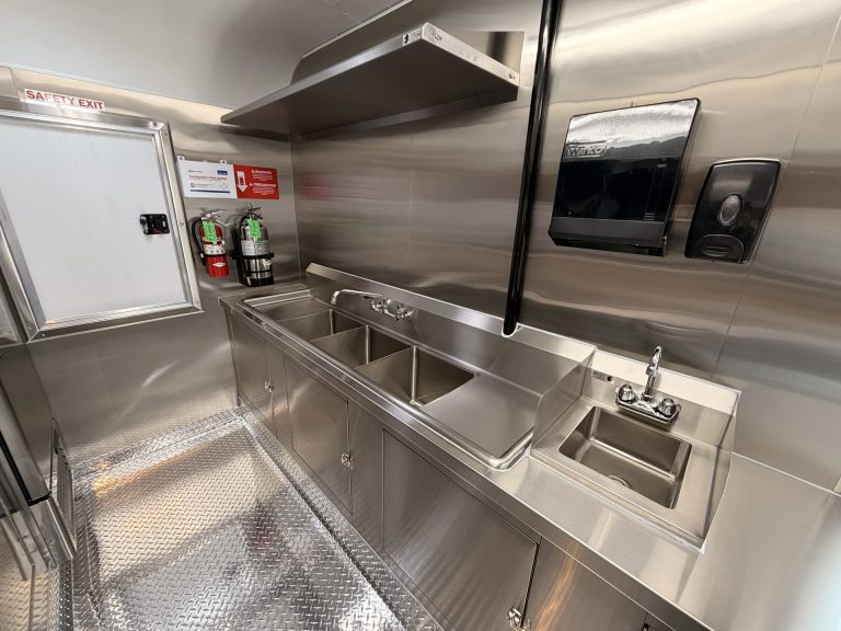 Stainless steel three-compartment sink and hand wash sink inside food trailer with commercial sanitation setup