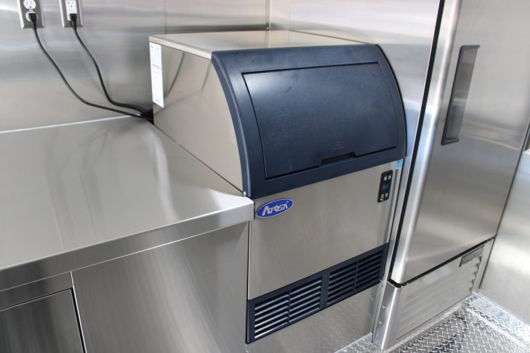 Undercounter ice maker integrated into the stainless steel preparation area inside the school food trailer.