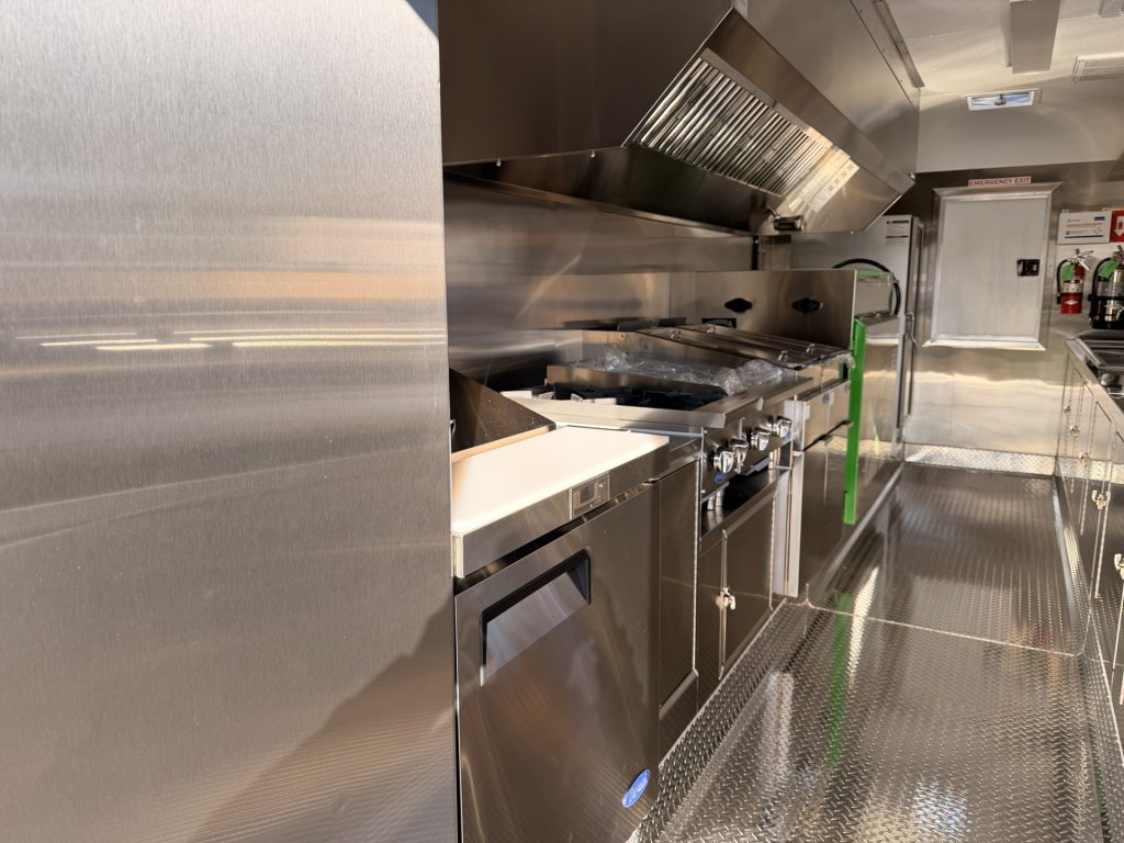 Commercial food trailer interior with cooking equipment, stainless steel countertops, and ventilation hood.