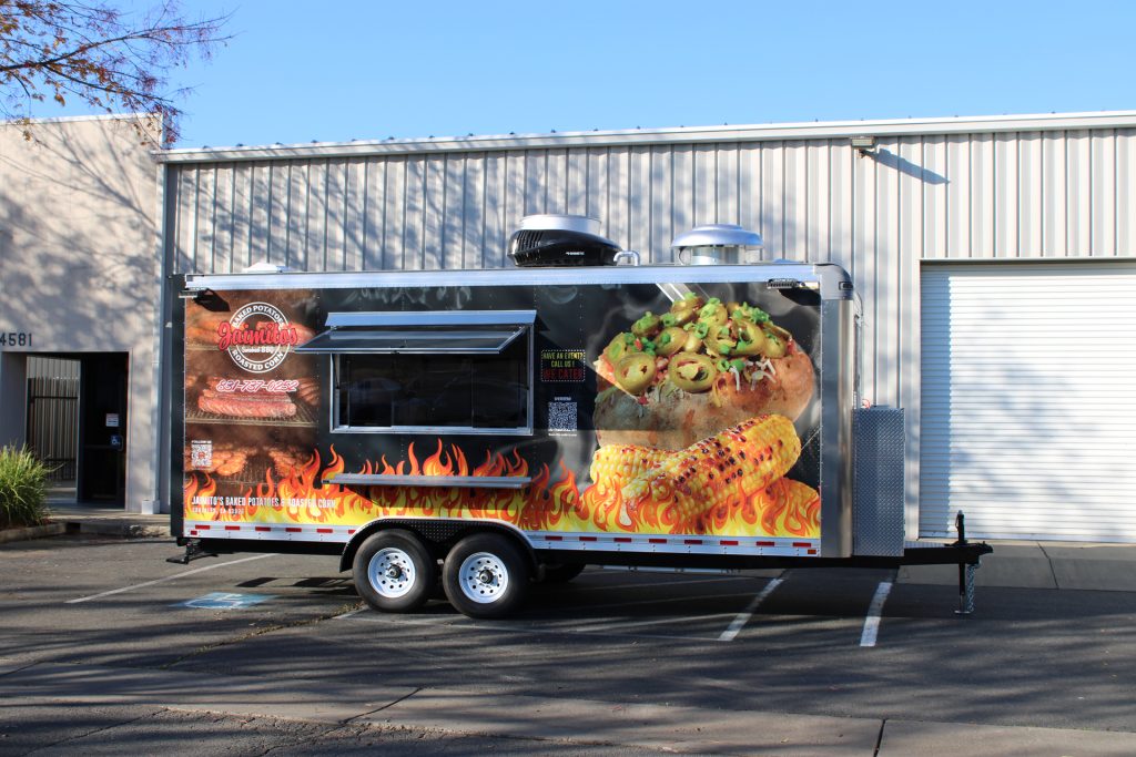 Black BBQ food trailer with colorful food graphics, serving window, and tandem axles.