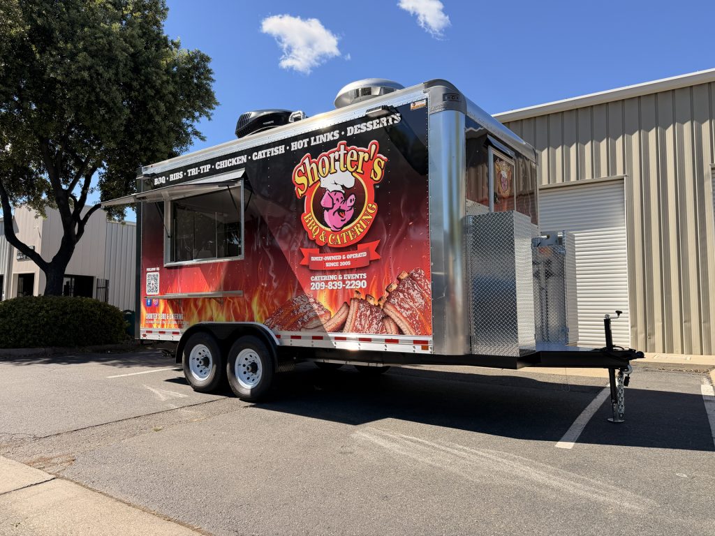 Black and red BBQ food trailer with barbecue-themed graphics, serving window, and tandem axles.