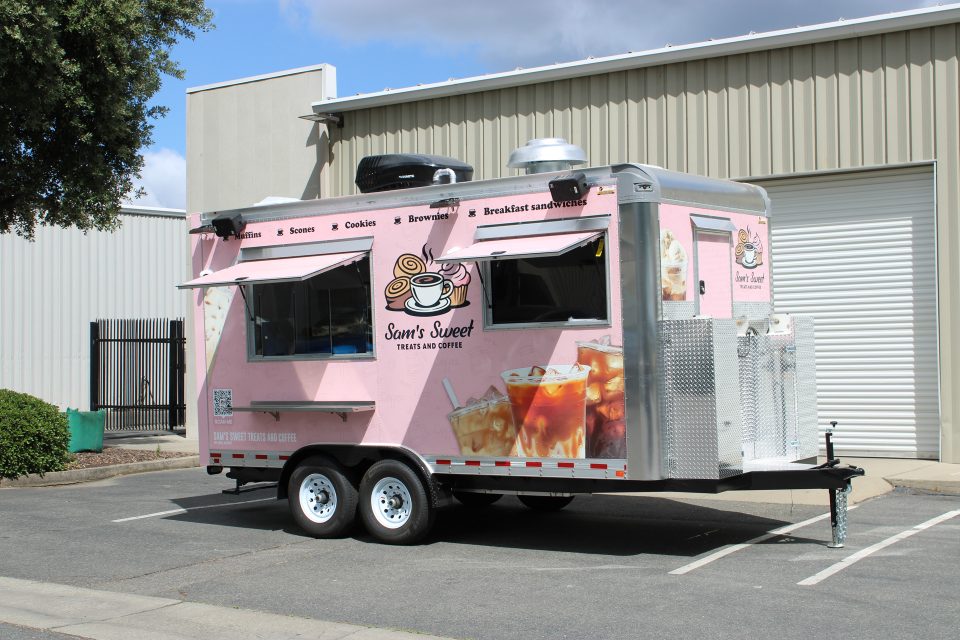 Pink custom coffee trailer with a branded vinyl wrap, side serving window, and tandem axles.