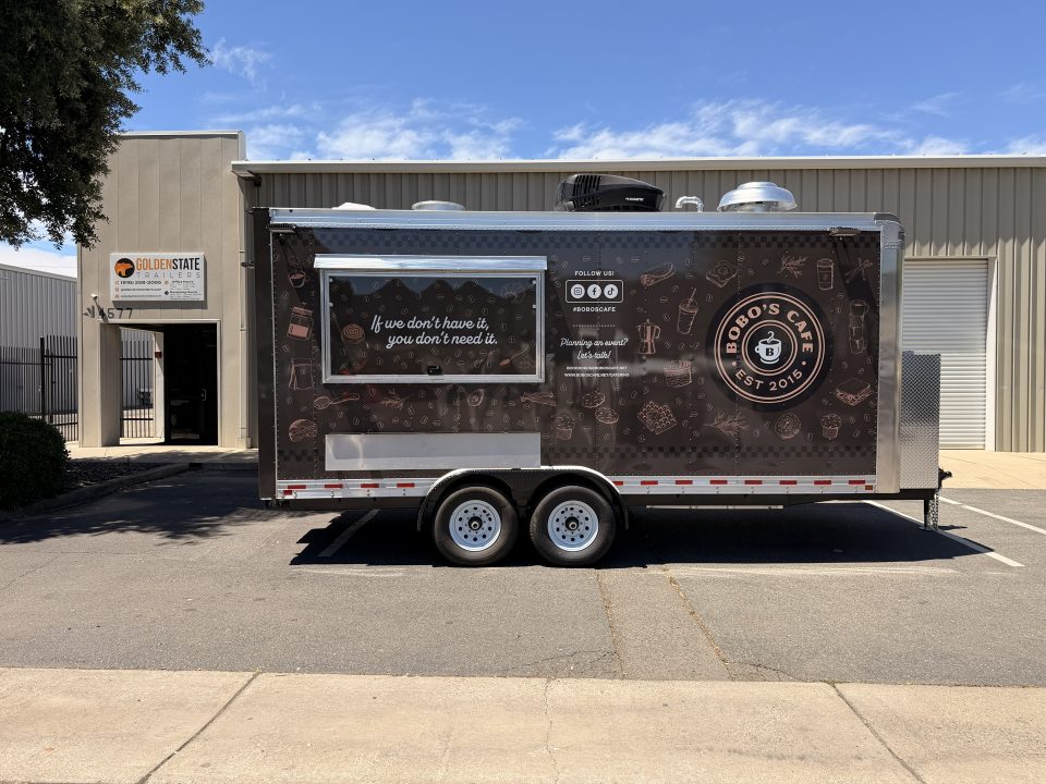 Dark brown custom coffee trailer with a branded exterior wrap, serving window, and tandem axles.