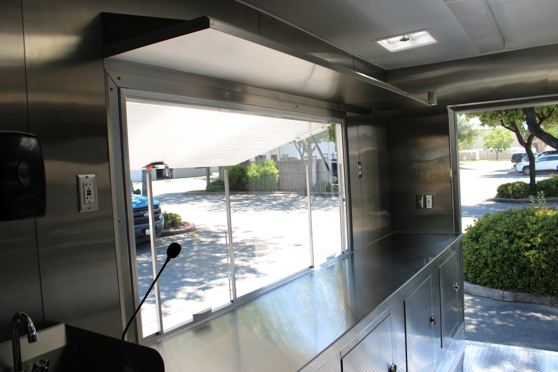 Coffee trailer service window with stainless steel counter and overhead shelving