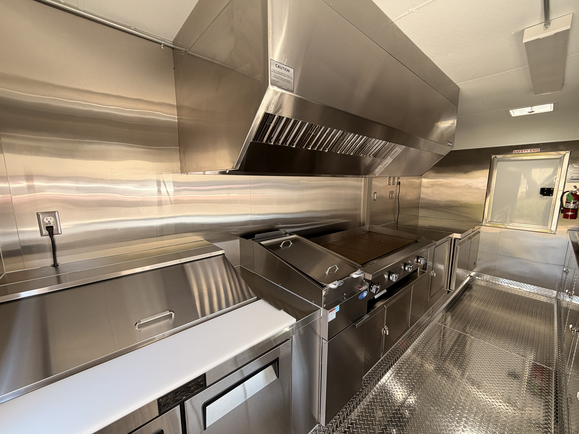 Inside a 16-foot taco food trailer with a commercial griddle, deep fryer, ventilation hood, and stainless steel work surfaces.