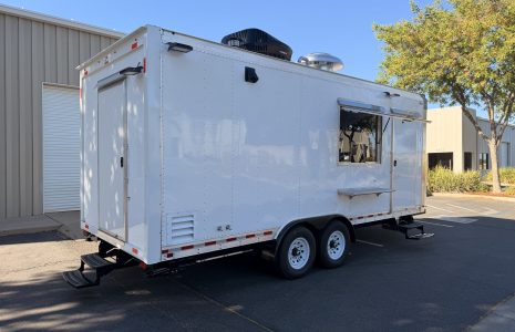 White custom commercial food trailer with serving windows, side entrance, and tandem axles parked outside the Golden State Trailers facility.