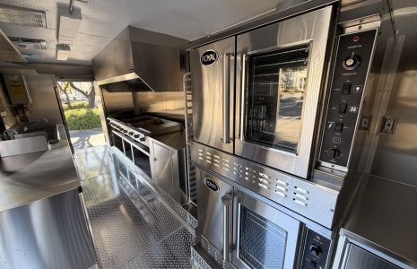 Interior of a 20-foot commercial food trailer with a convection oven, cooking line, exhaust hood, and stainless steel workstations.