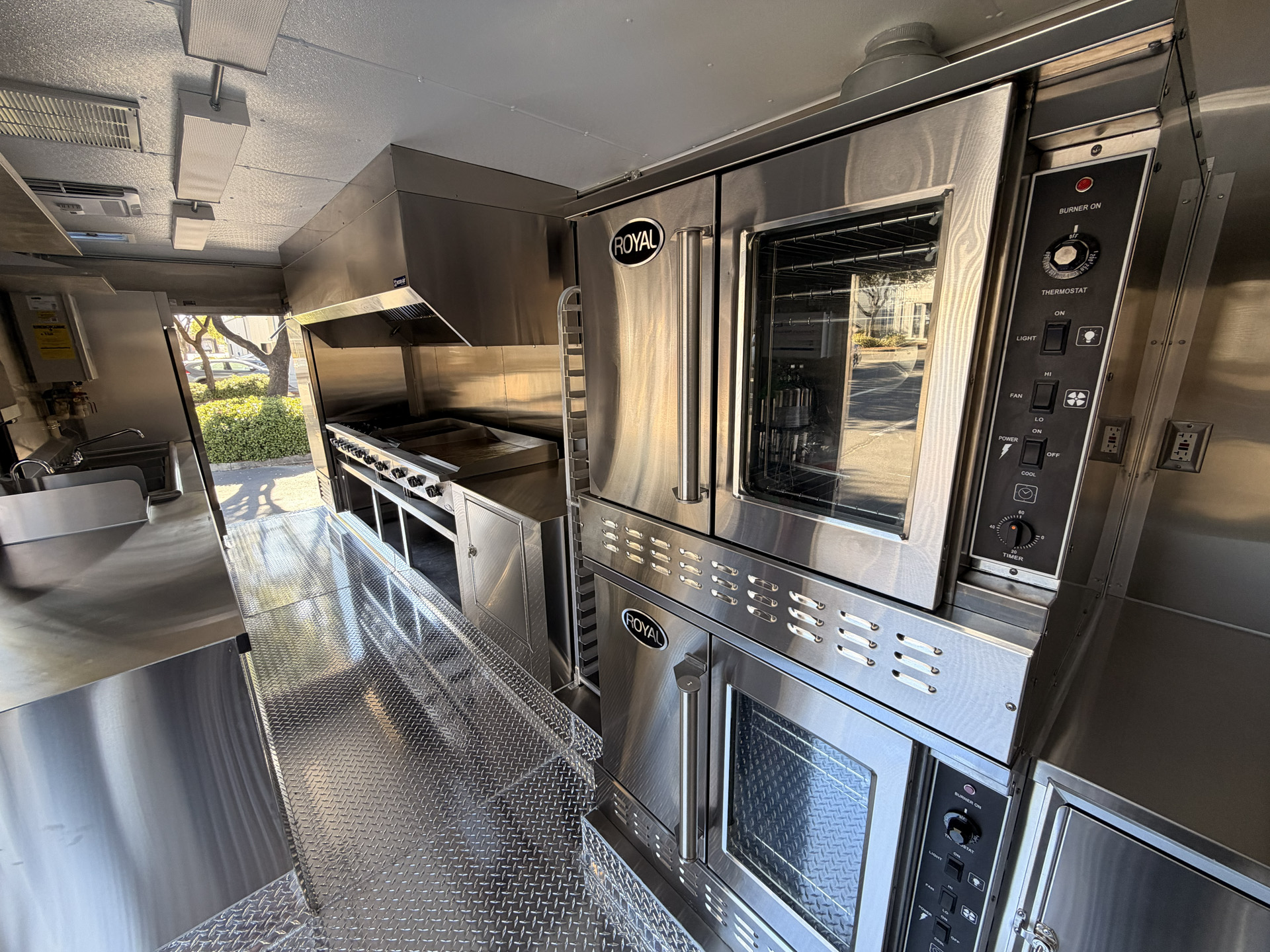 Interior of a 20-foot commercial food trailer with a convection oven, cooking line, exhaust hood, and stainless steel workstations.