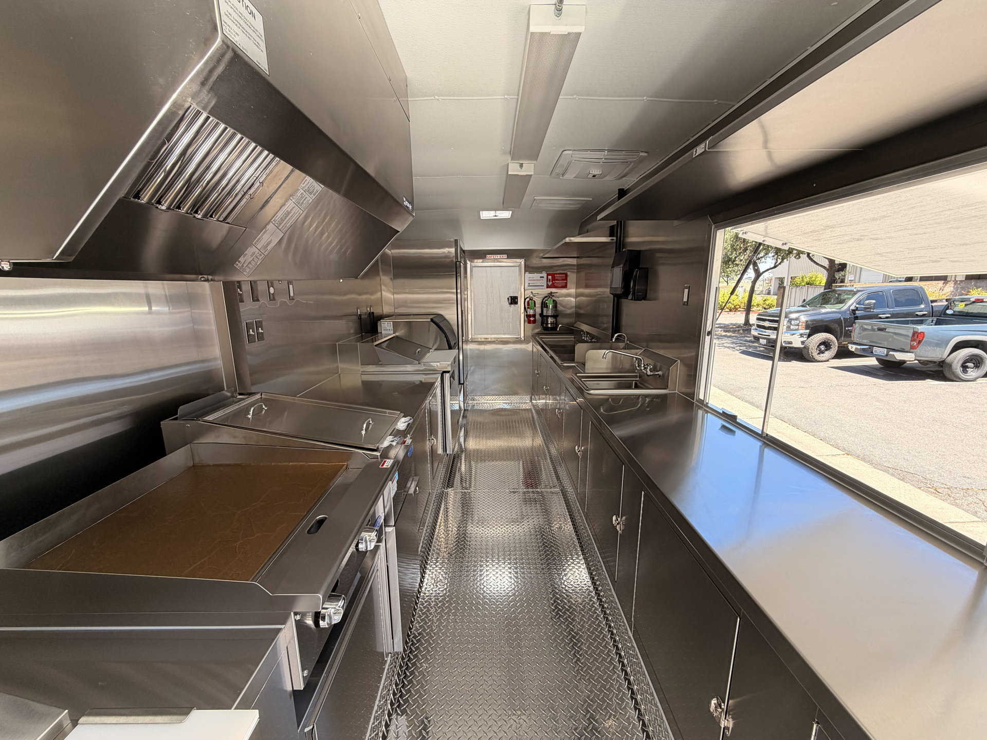 Interior of an 18-foot food trailer with a commercial cooking line, stainless steel counters, sinks, and serving window.