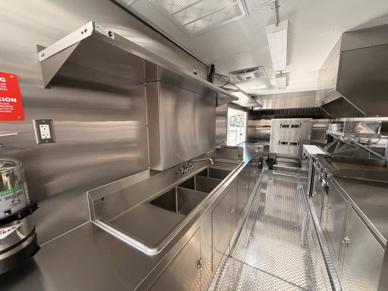 commercial pizza food trailer interior with stainless steel work surfaces, service window, cooking line, and central aisle