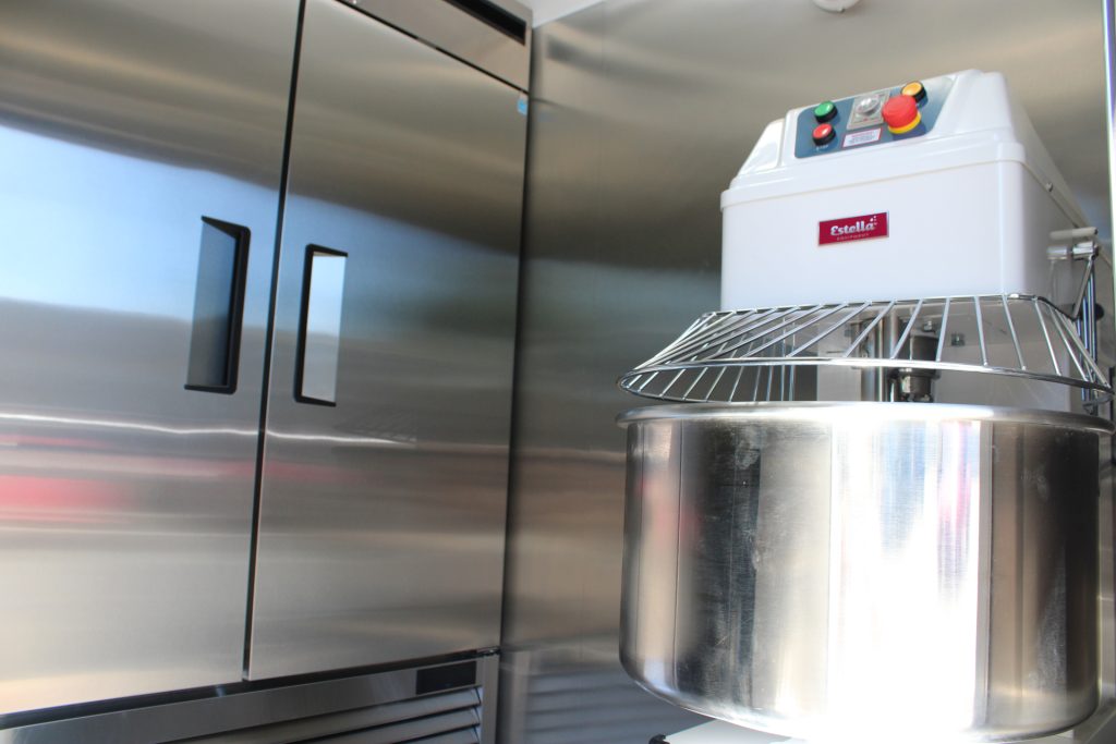 Commercial spiral dough mixer and refrigeration inside a custom pizza food trailer.