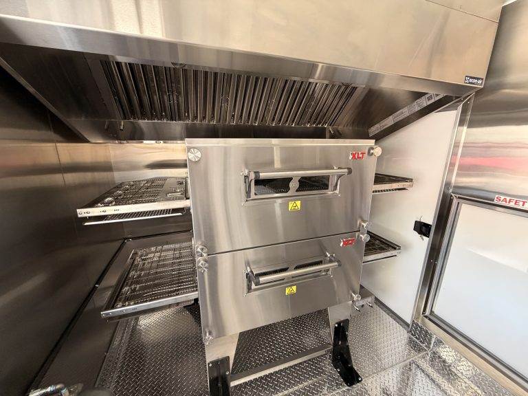 double-stack conveyor pizza oven inside a commercial pizza food trailer with stainless steel interior and ventilation hood