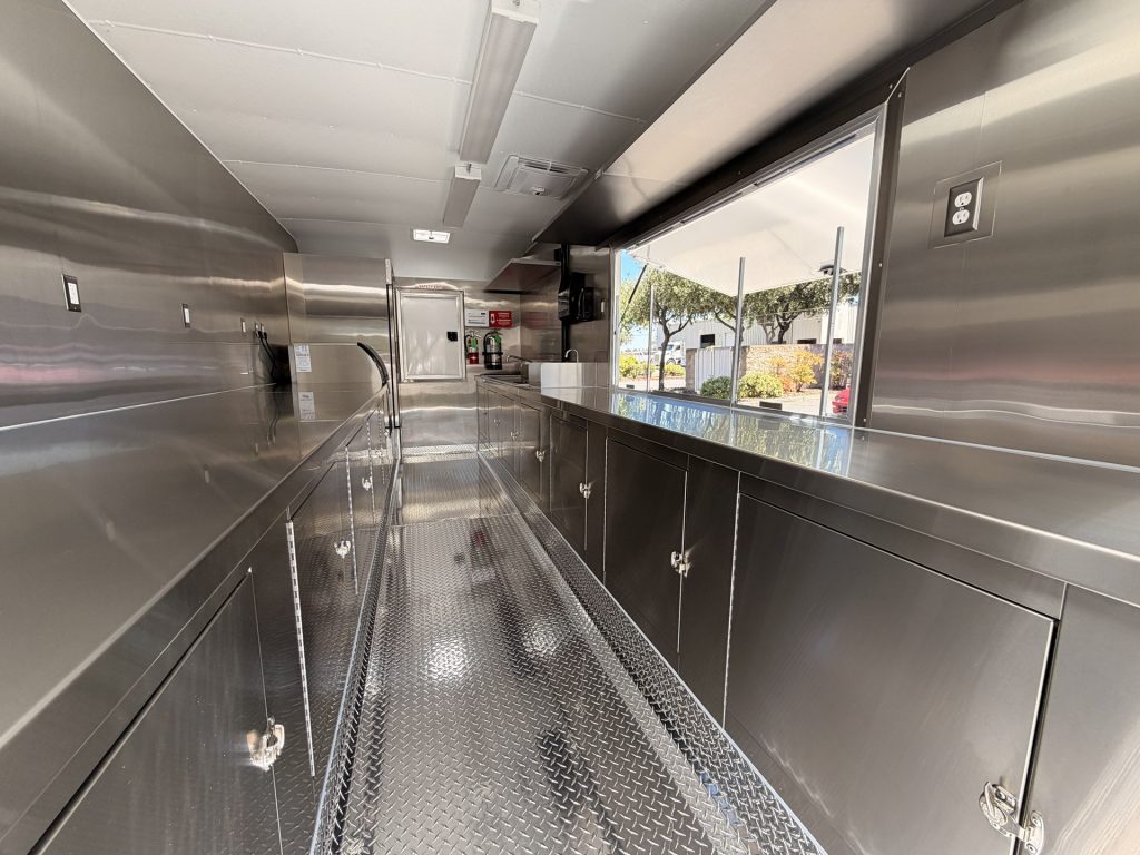 Interior storage, stainless steel counters, and central workflow aisle inside the Reef-Sunset school food trailer