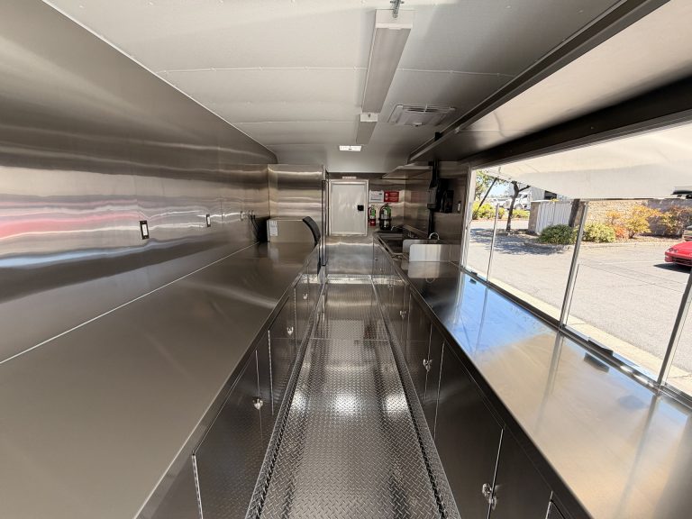 School food trailer kitchen with stainless steel counters, enclosed cabinets, and service window