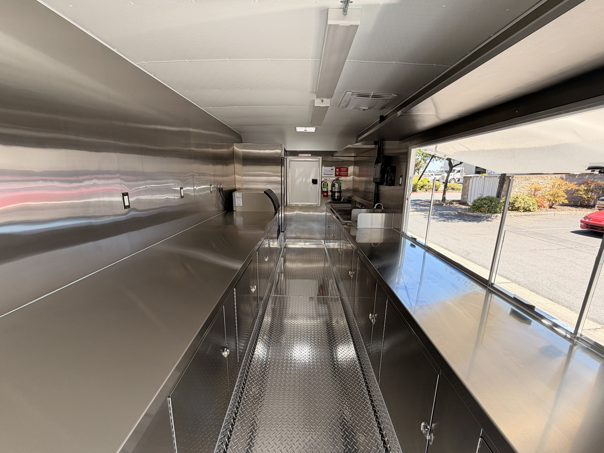 School food trailer kitchen with stainless steel counters, enclosed cabinets, and service window